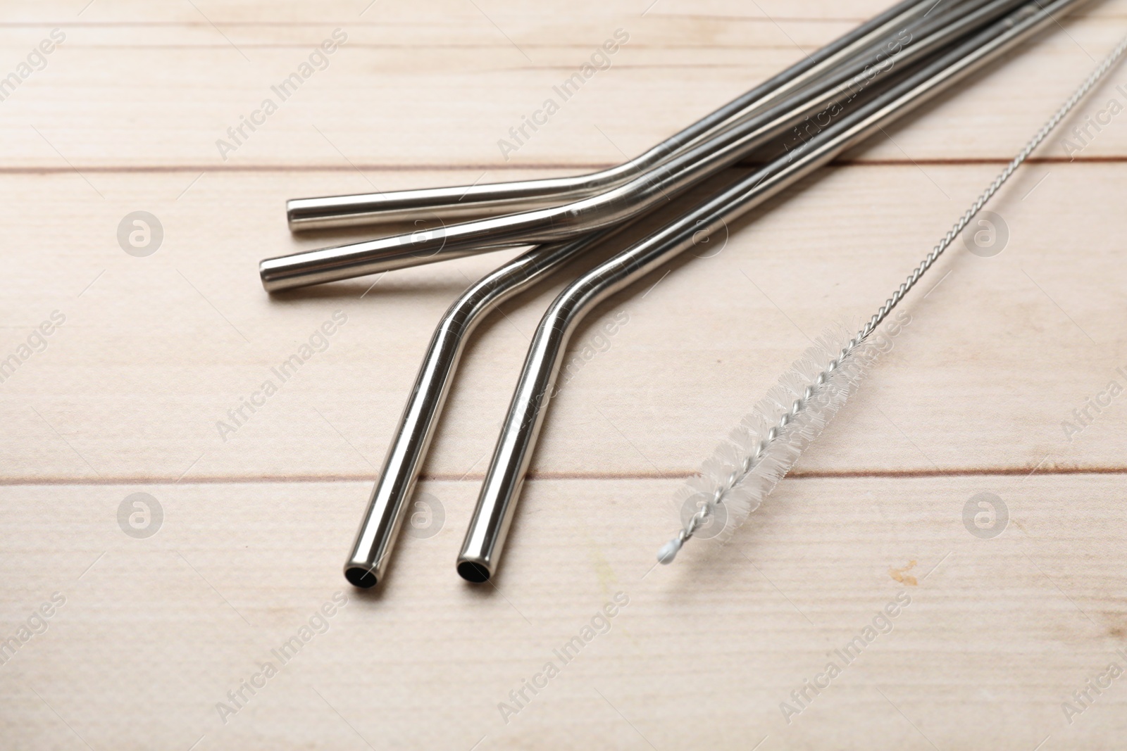 Photo of Metal drinking straws and cleaning brush on wooden table, closeup