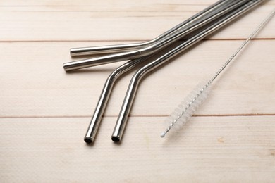 Photo of Metal drinking straws and cleaning brush on wooden table, closeup