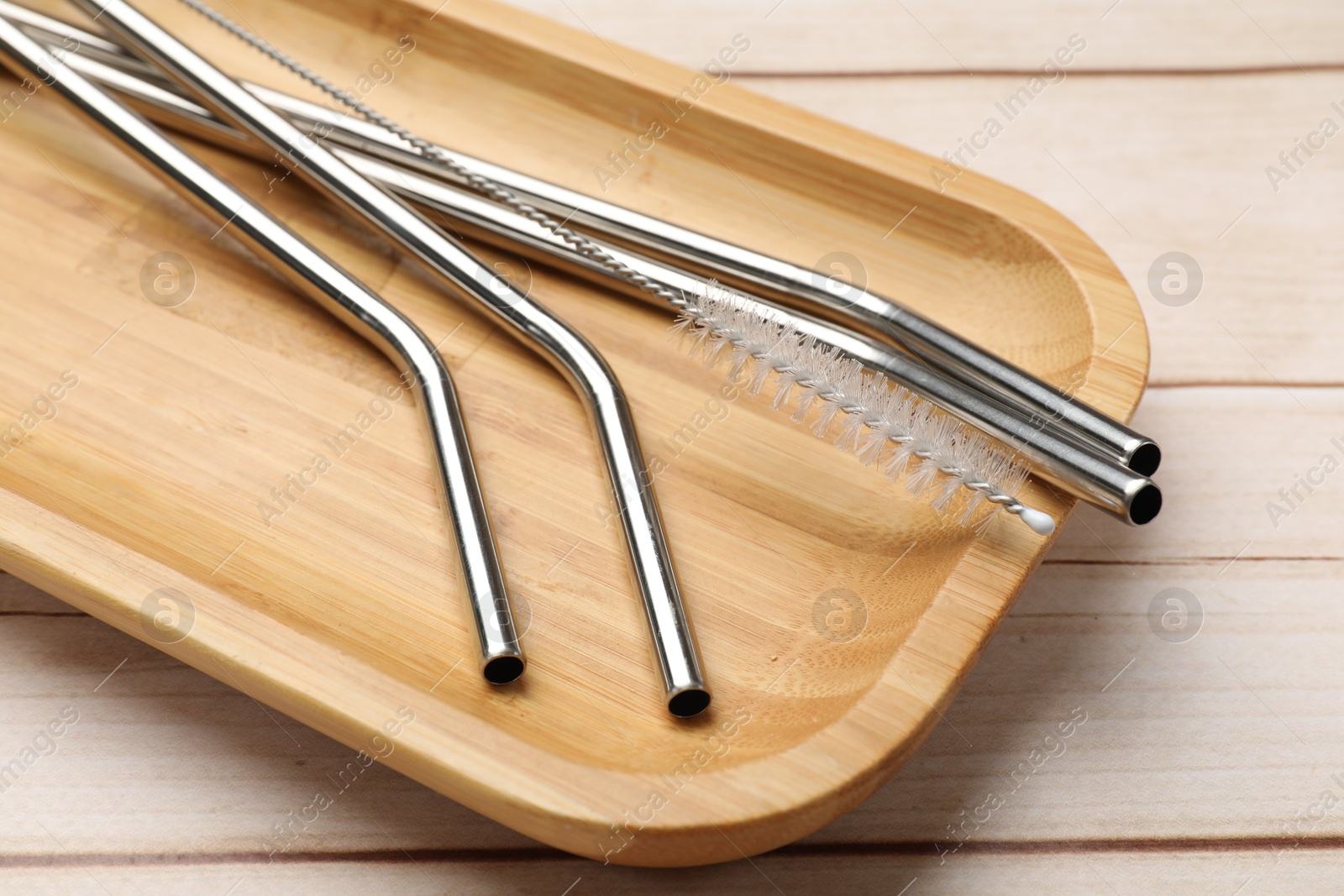 Photo of Metal drinking straws and cleaning brush on wooden table, closeup