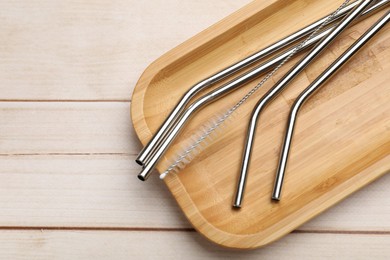 Photo of Metal drinking straws and cleaning brush on wooden table, top view