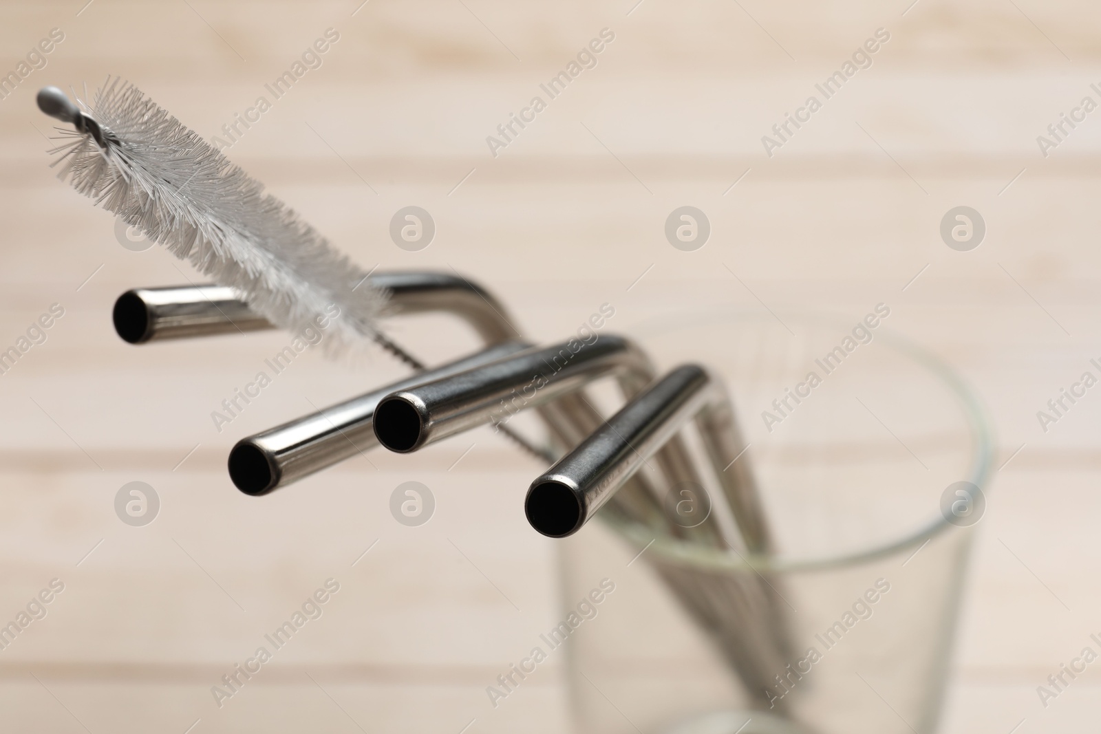 Photo of Metal drinking straws and cleaning brush in glass on beige table, closeup