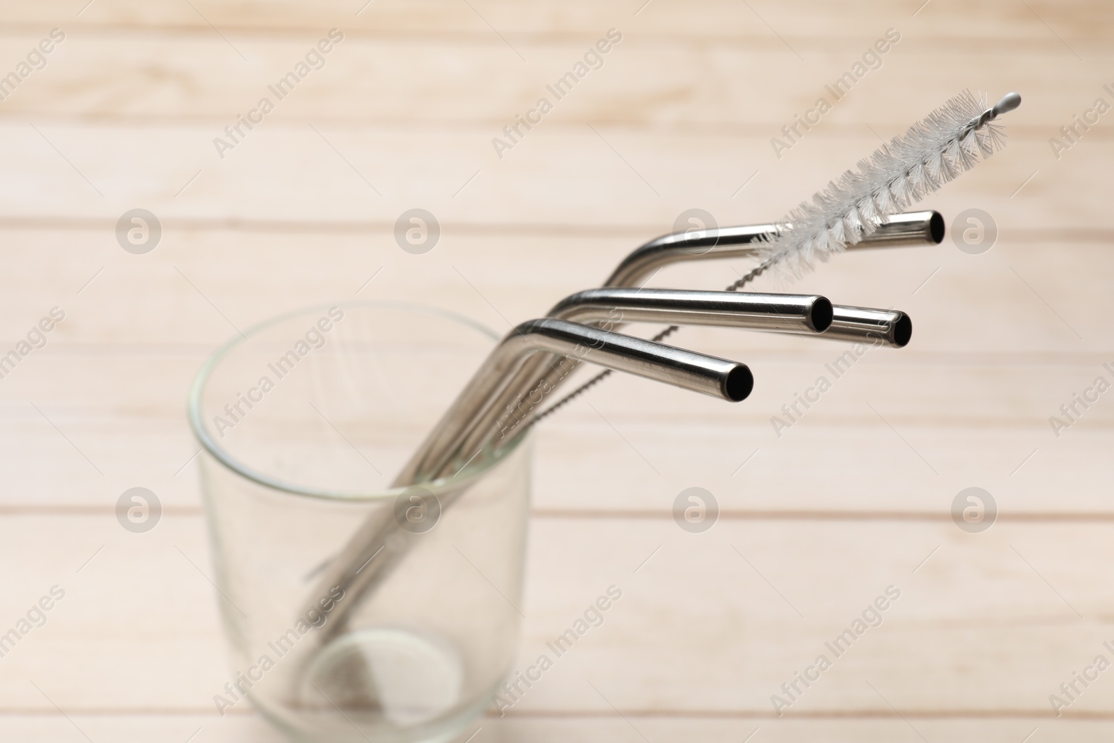 Photo of Metal drinking straws and cleaning brush in glass on wooden table, closeup