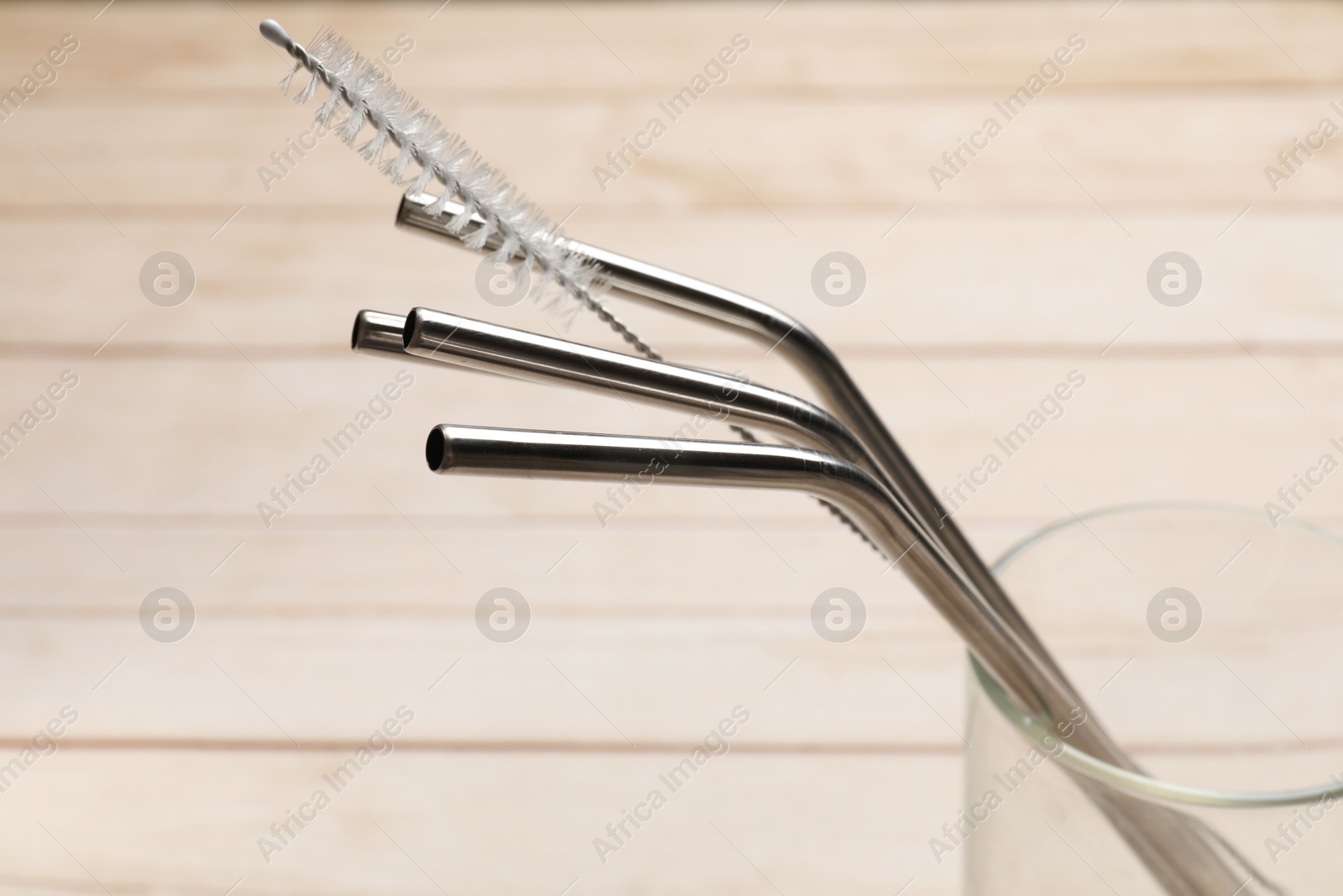 Photo of Metal drinking straws and cleaning brush in glass on wooden table, closeup