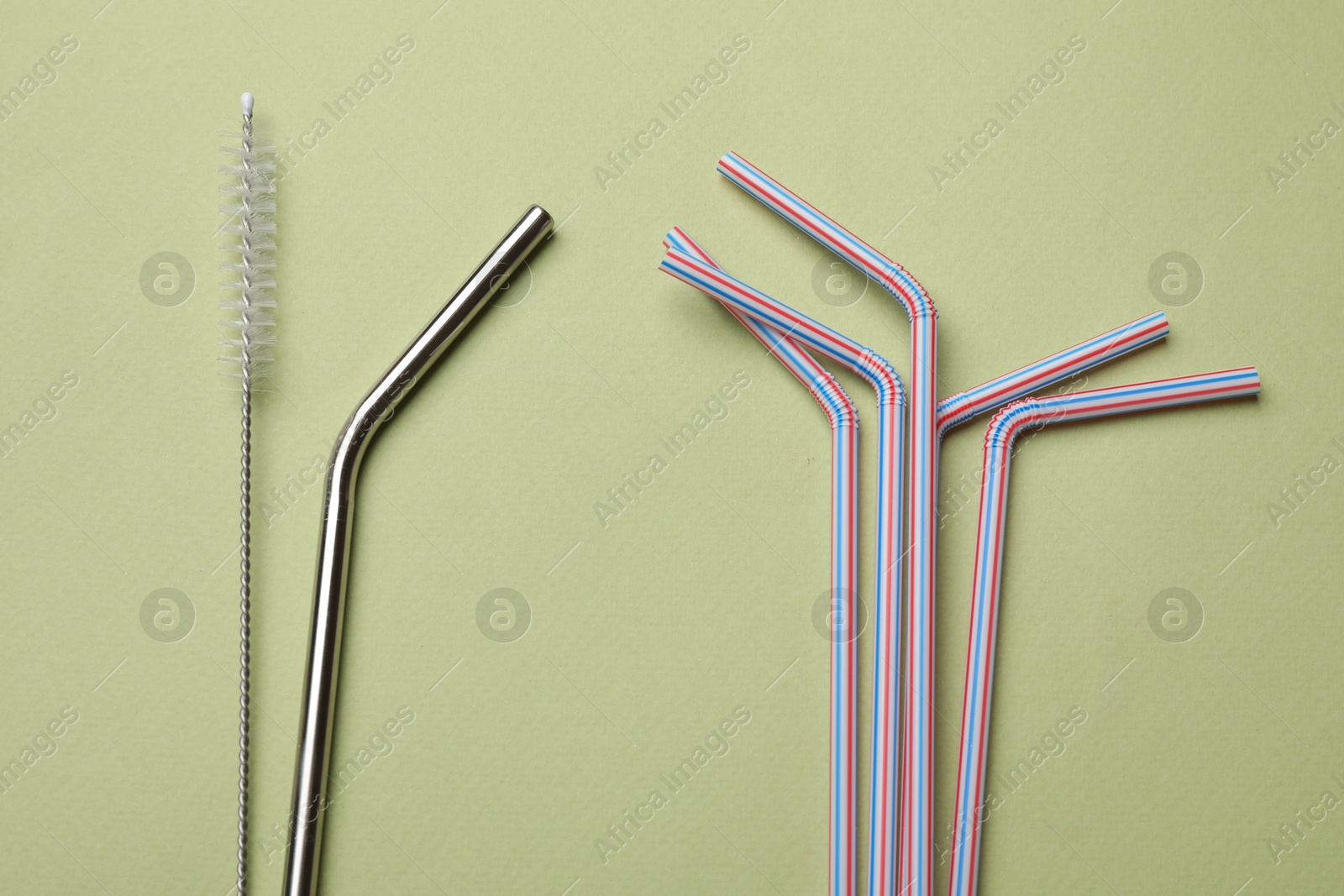 Photo of Different drinking straws and cleaning brush on green background, flat lay