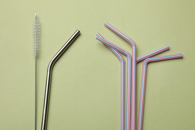 Photo of Different drinking straws and cleaning brush on green background, flat lay