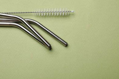 Photo of Metal drinking straws and cleaning brush on green background, top view. Space for text