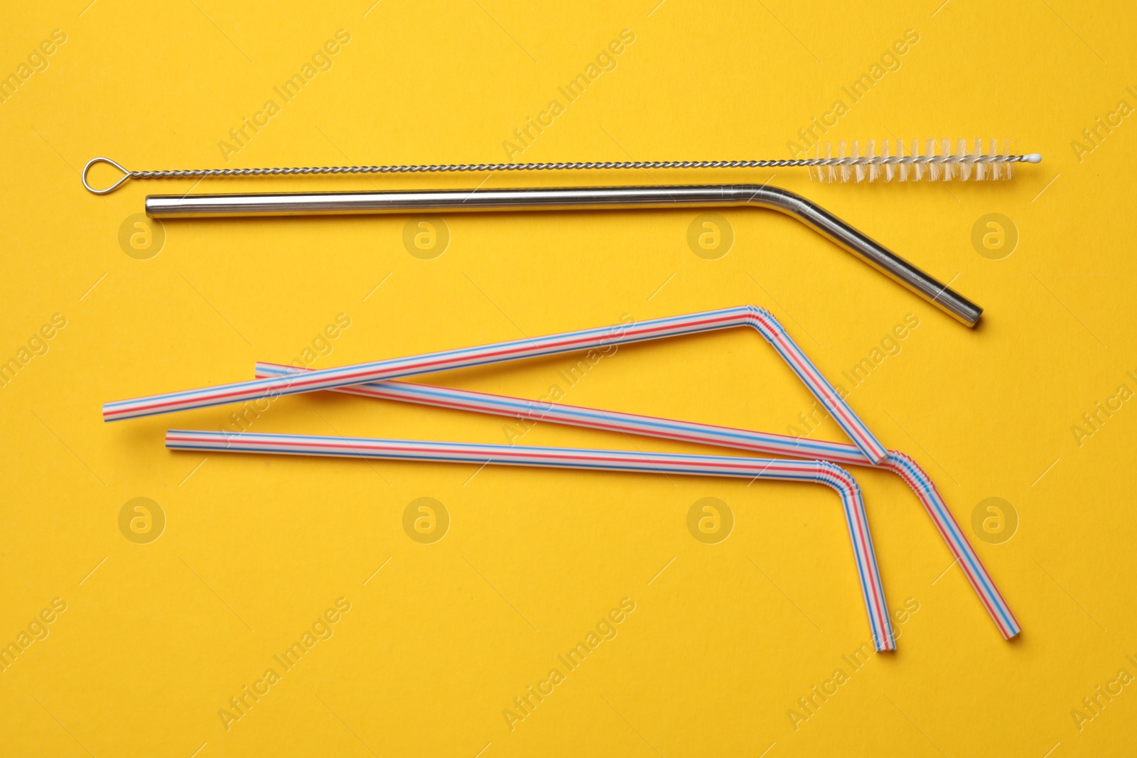 Photo of Different drinking straws and cleaning brush on yellow background, flat lay