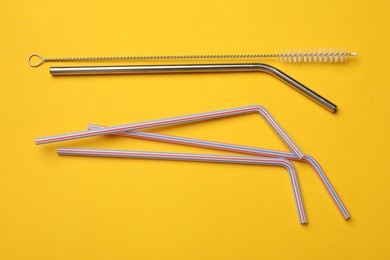 Photo of Different drinking straws and cleaning brush on yellow background, flat lay