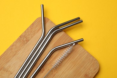 Photo of Metal drinking straws and cleaning brush on yellow background, top view