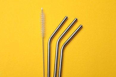 Photo of Metal drinking straws and cleaning brush on yellow background, flat lay