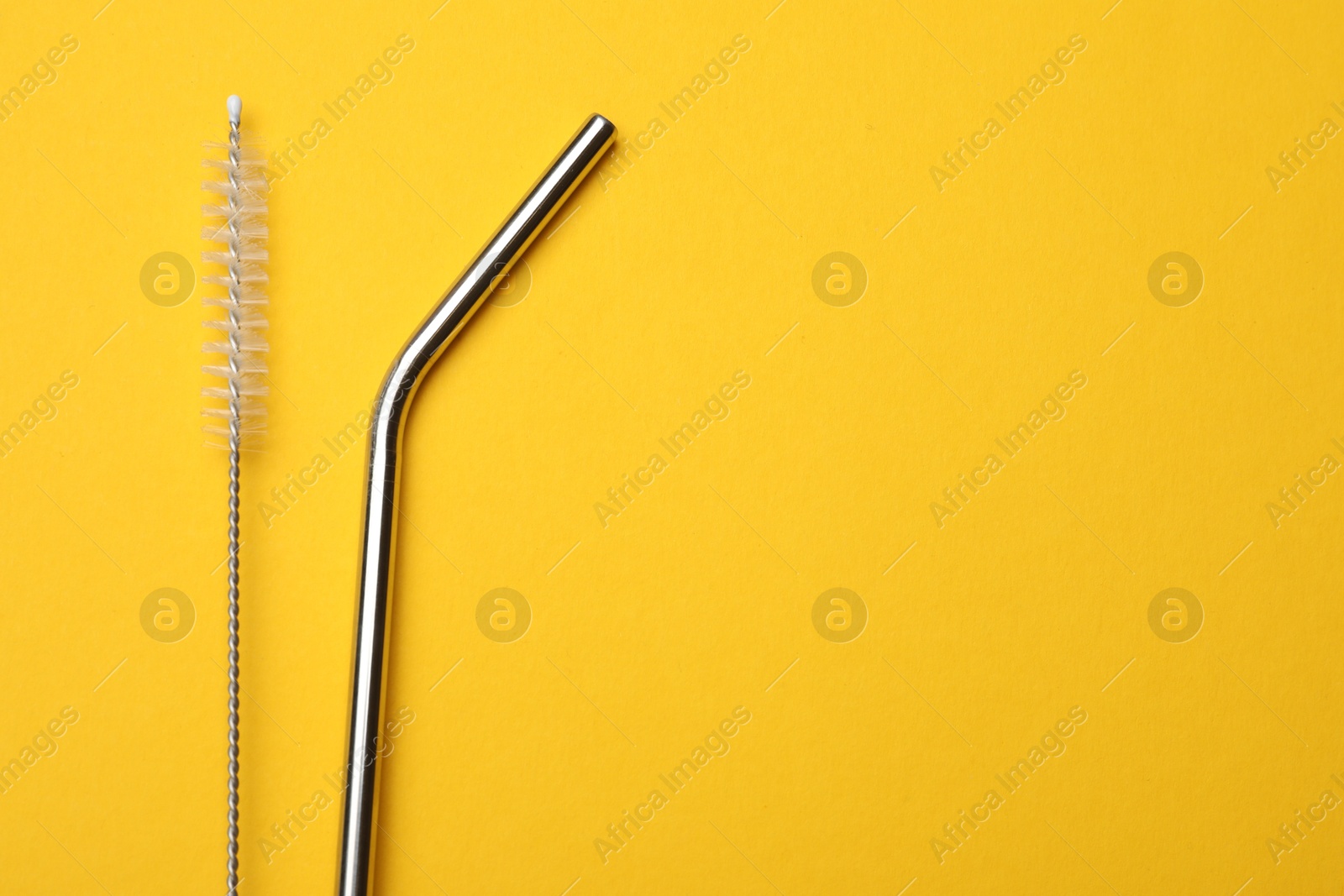 Photo of Metal drinking straws and cleaning brush on yellow background, flat lay. Space for text