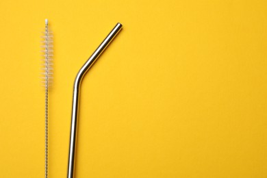 Photo of Metal drinking straws and cleaning brush on yellow background, flat lay. Space for text