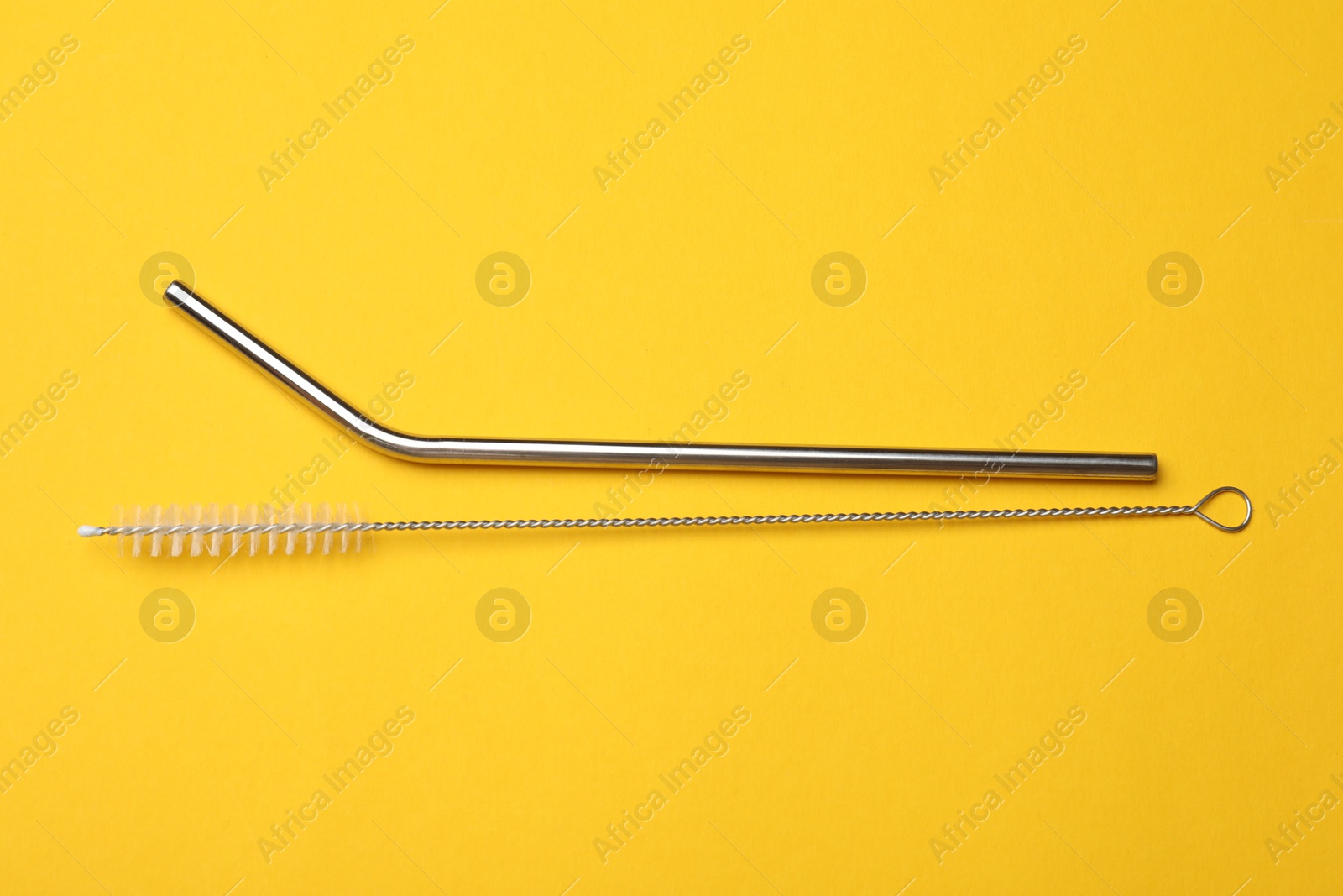 Photo of Metal drinking straws and cleaning brush on yellow background, flat lay