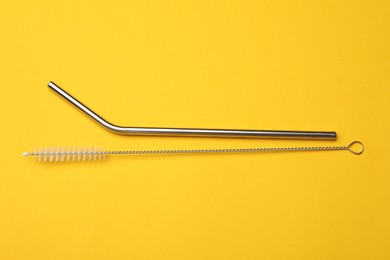 Photo of Metal drinking straws and cleaning brush on yellow background, flat lay