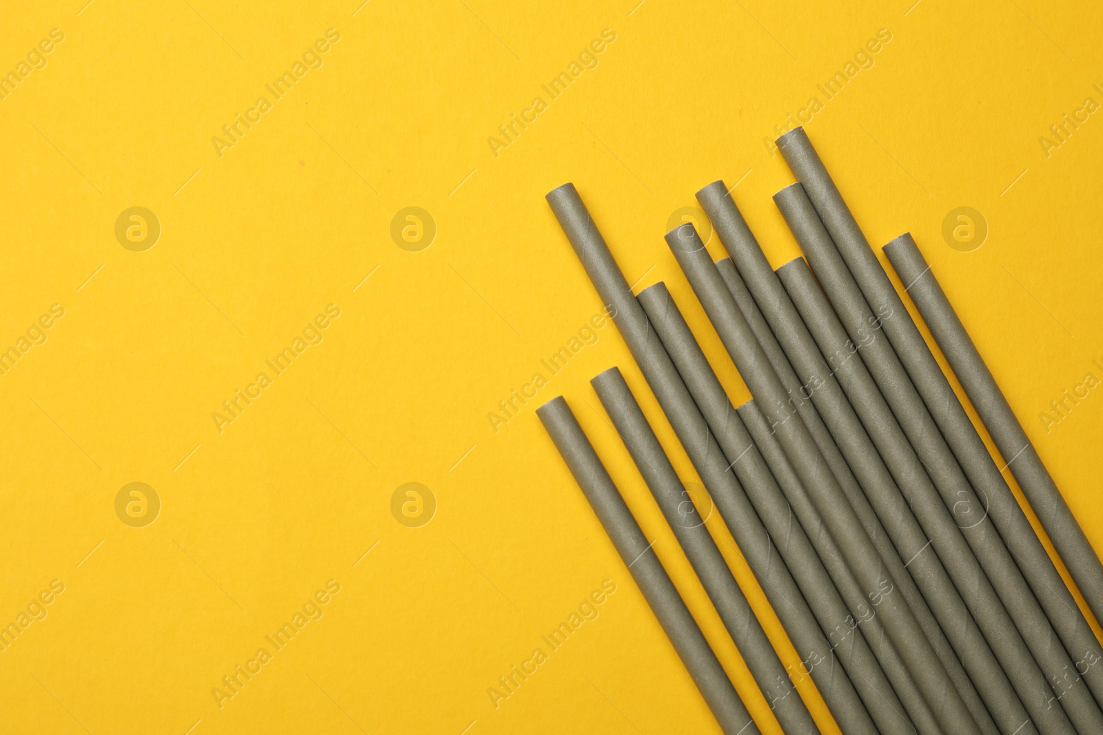 Photo of Bamboo drinking straws on yellow background, top view. Space for text