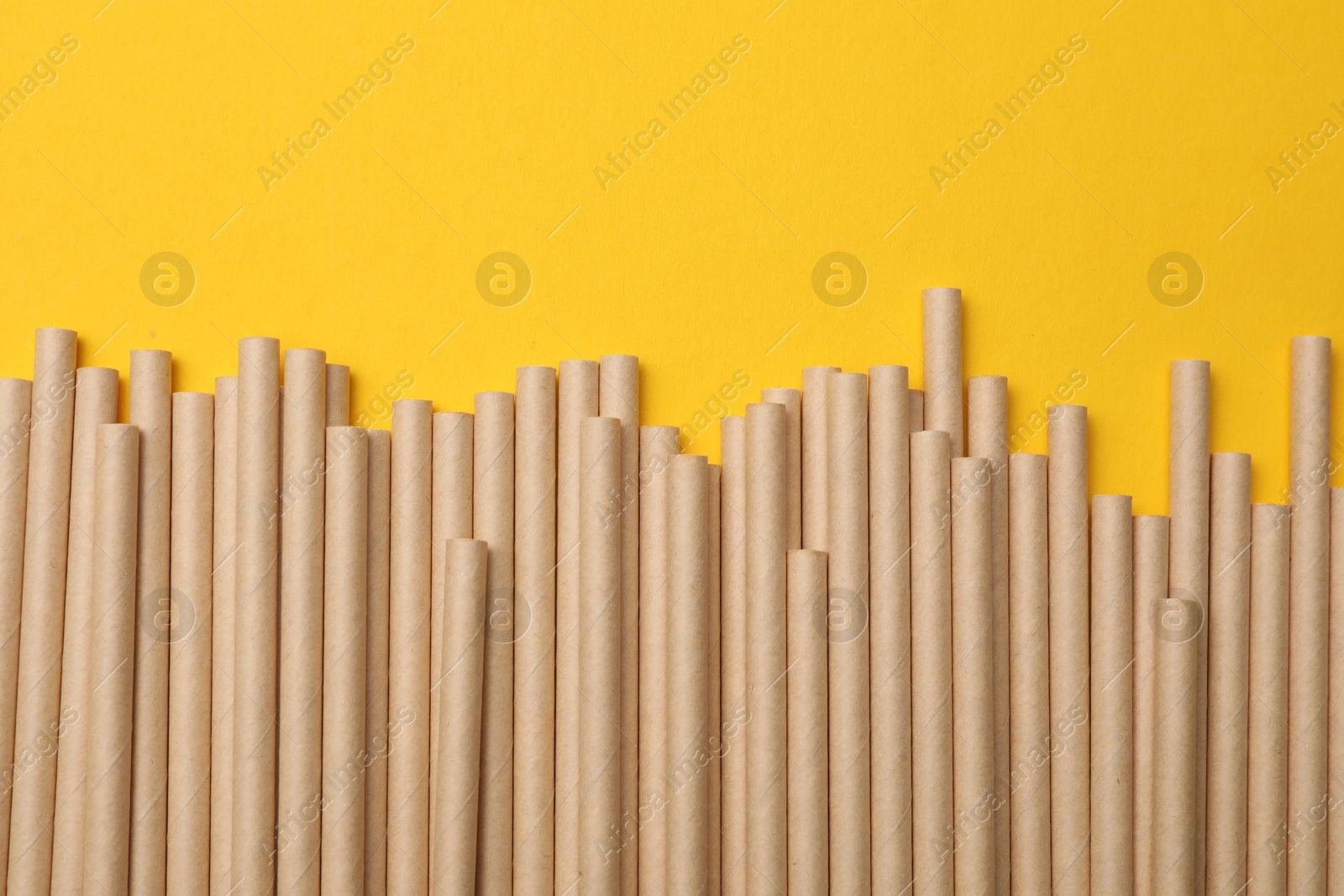 Photo of Bamboo drinking straws on yellow background, top view. Space for text