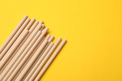 Photo of Bamboo drinking straws on yellow background, top view. Space for text