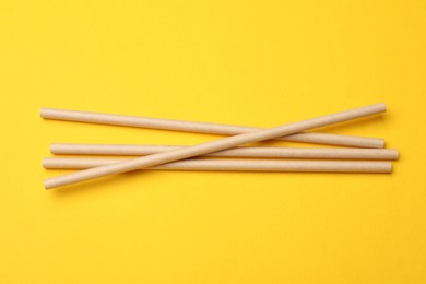 Photo of Bamboo drinking straws on yellow background, top view