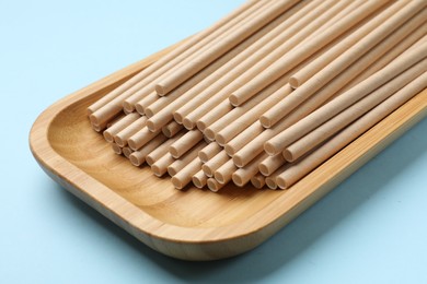 Photo of Bamboo drinking straws on light blue background, closeup