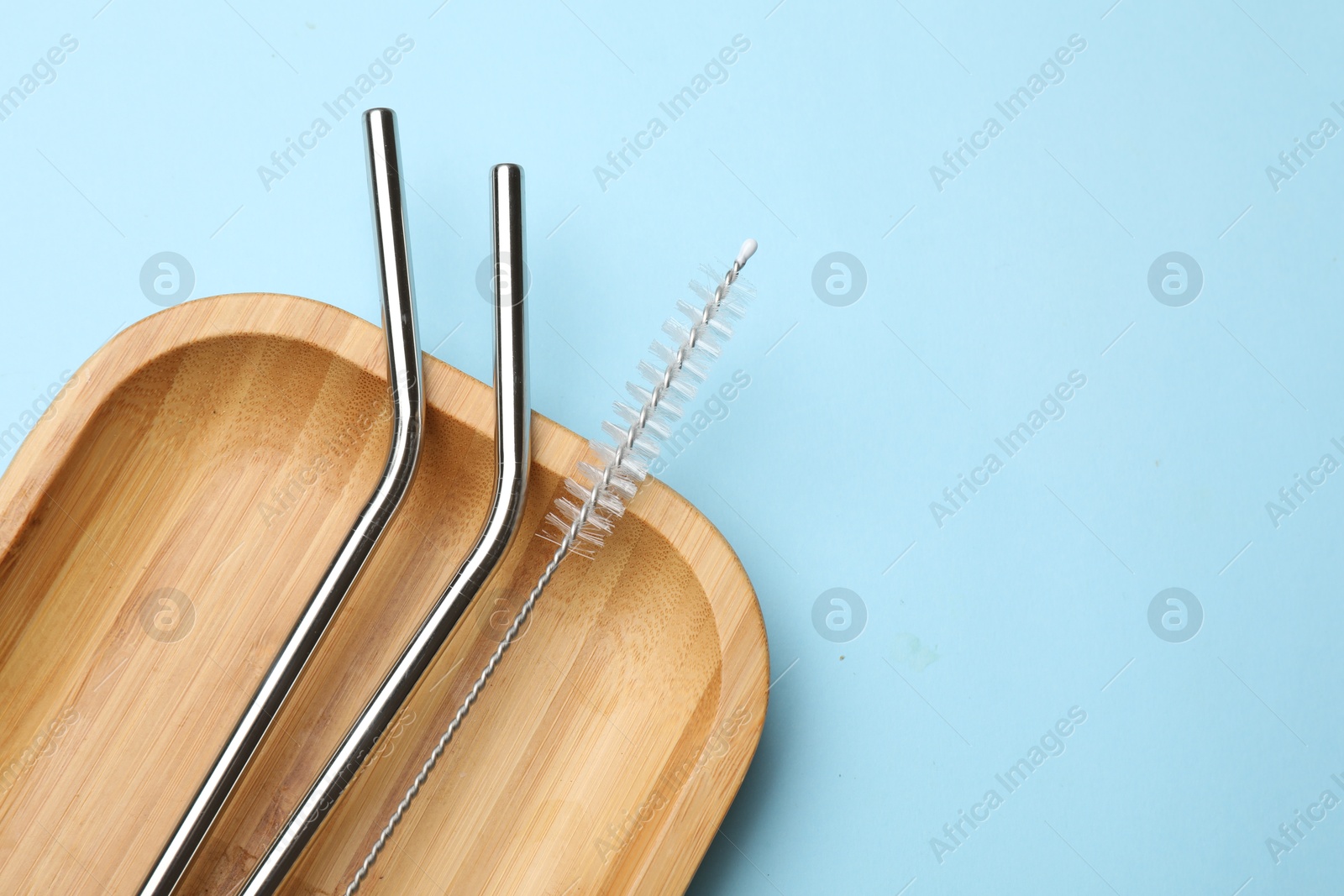 Photo of Metal drinking straws and cleaning brush on light blue background, top view. Space for text