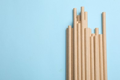 Photo of Bamboo drinking straws on light blue background, top view. Space for text