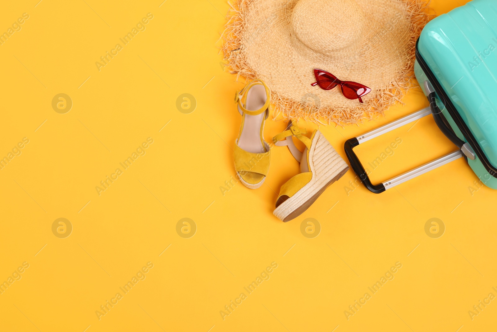 Photo of Turquoise suitcase, straw hat, shoes and sunglasses on yellow background, above view. Space for text