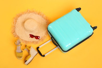 Photo of Turquoise suitcase, straw hat, shoes and sunglasses on yellow background, above view