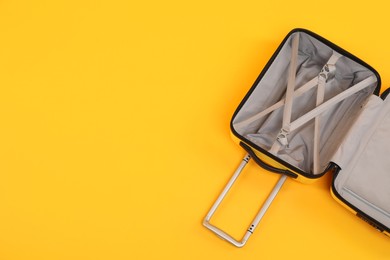 Photo of Open empty suitcase on yellow background, top view. Space for text