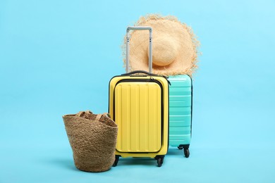 Suitcases with straw hat and bag on light blue background