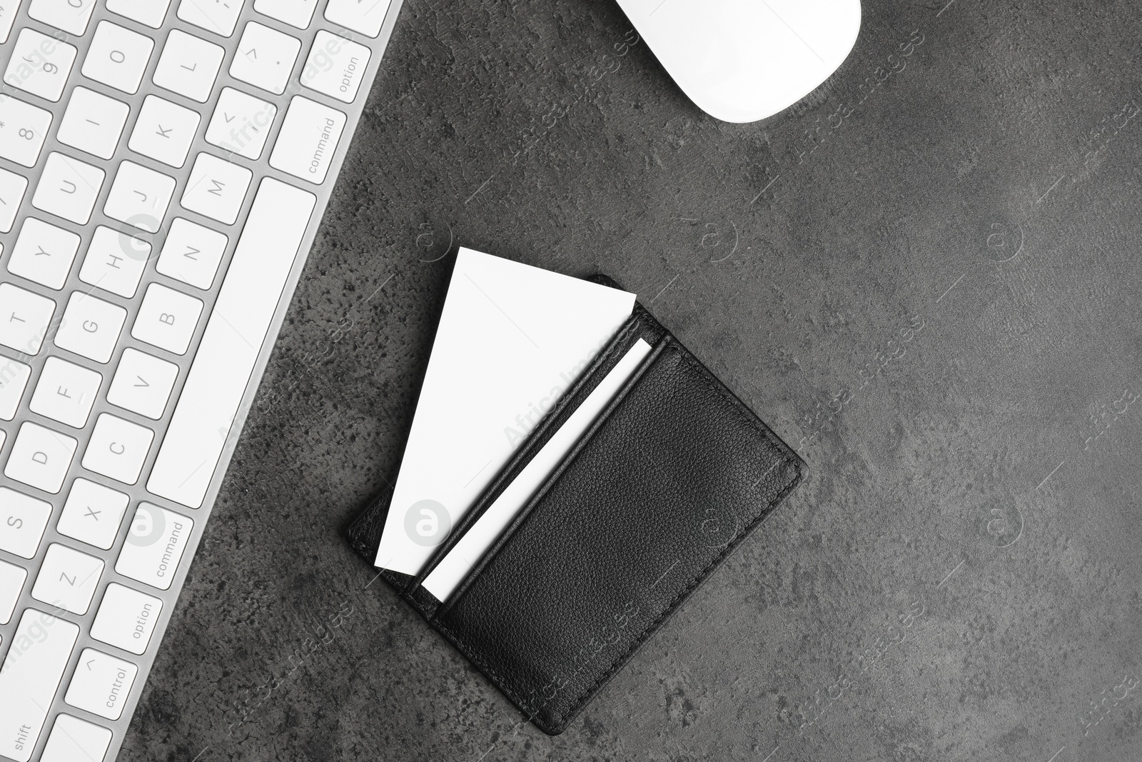 Photo of Leather card holder with blank business cards, mouse and keyboard on grey textured table, flat lay