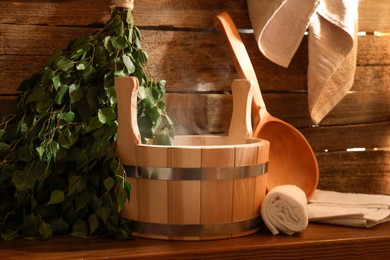 Photo of Sauna equipment. Bucket, ladle, birch whisk and towels on wooden table indoors