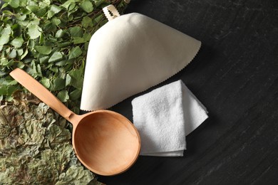 Photo of Sauna whisks, felt wool hat, ladle and towel on black textured surface, flat lay