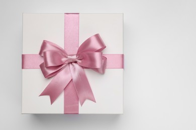 Photo of Gift box with pink bow on light grey background, top view. Space for text