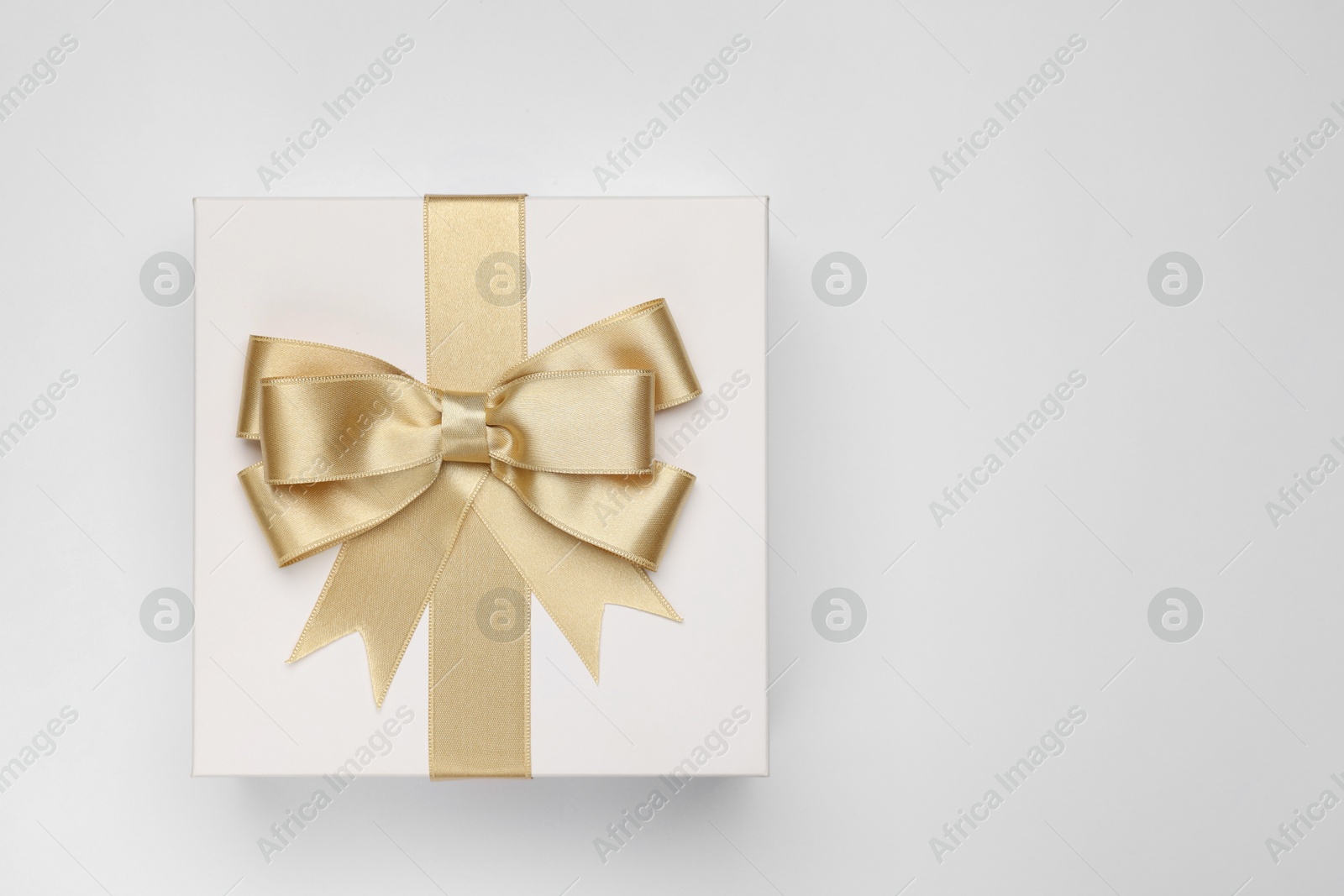 Photo of Gift box with golden bow on light grey background, top view. Space for text