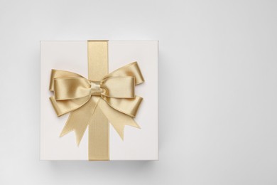 Photo of Gift box with golden bow on light grey background, top view. Space for text