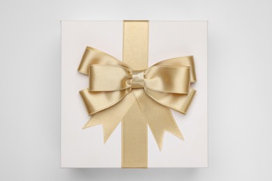 Gift box with golden bow on light grey background, top view