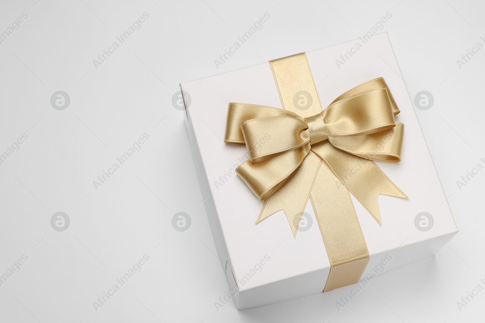 Photo of Gift box with golden bow on light grey background, above view. Space for text