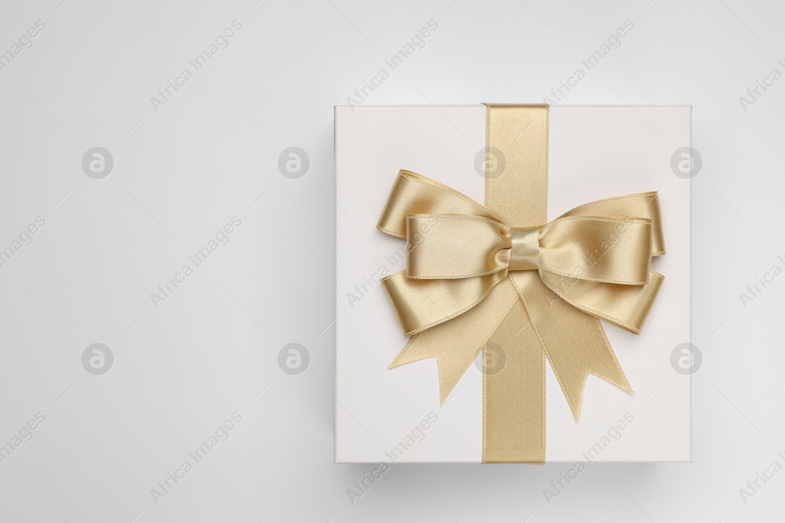 Photo of Gift box with golden bow on light grey background, top view. Space for text