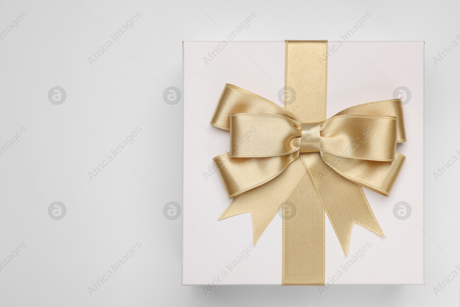 Photo of Gift box with golden bow on light grey background, top view. Space for text