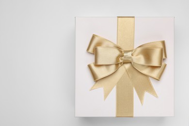 Photo of Gift box with golden bow on light grey background, top view. Space for text