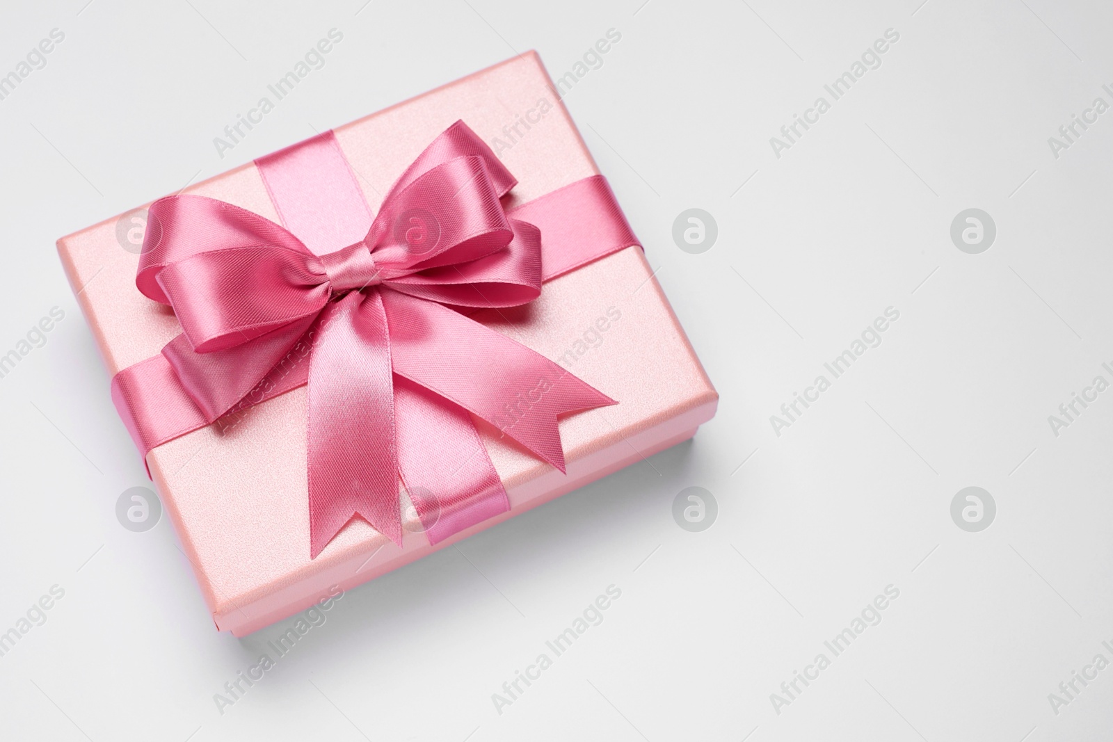 Photo of Gift box with pink bow on light grey background, top view. Space for text