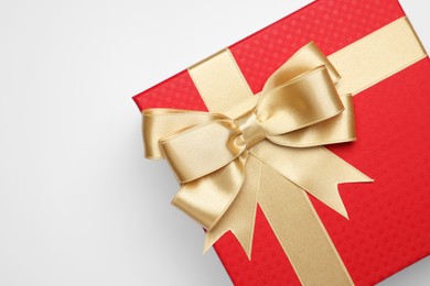 Gift box with golden bow on light grey background, top view. Space for text