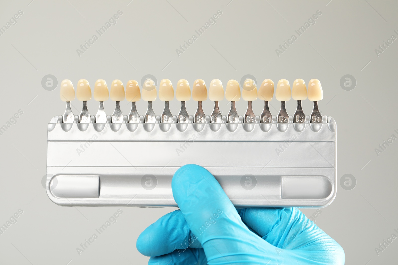 Photo of Doctor with teeth color chart on gray background, closeup. Dental veneers