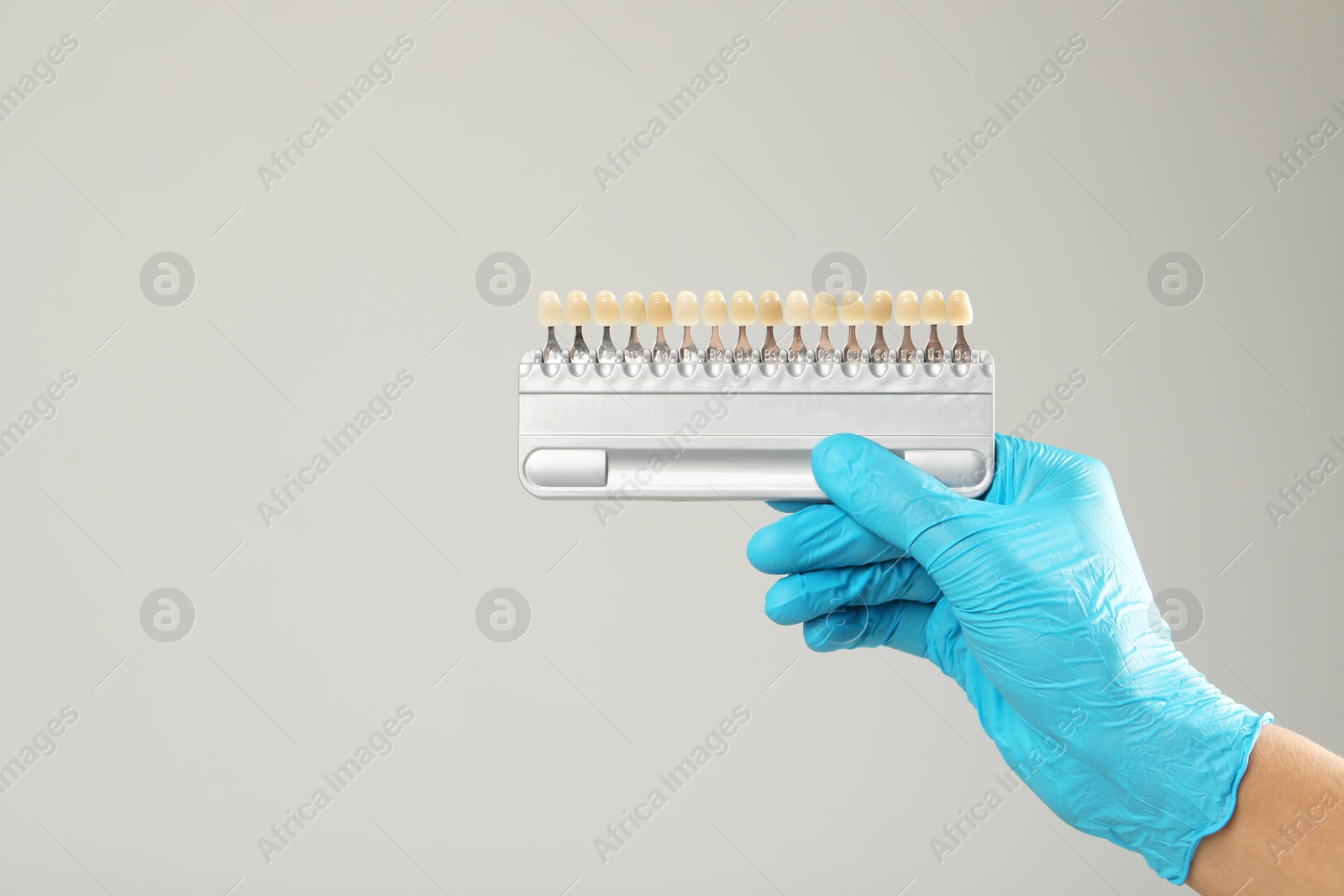 Photo of Doctor with teeth color chart on gray background, closeup. Dental veneers