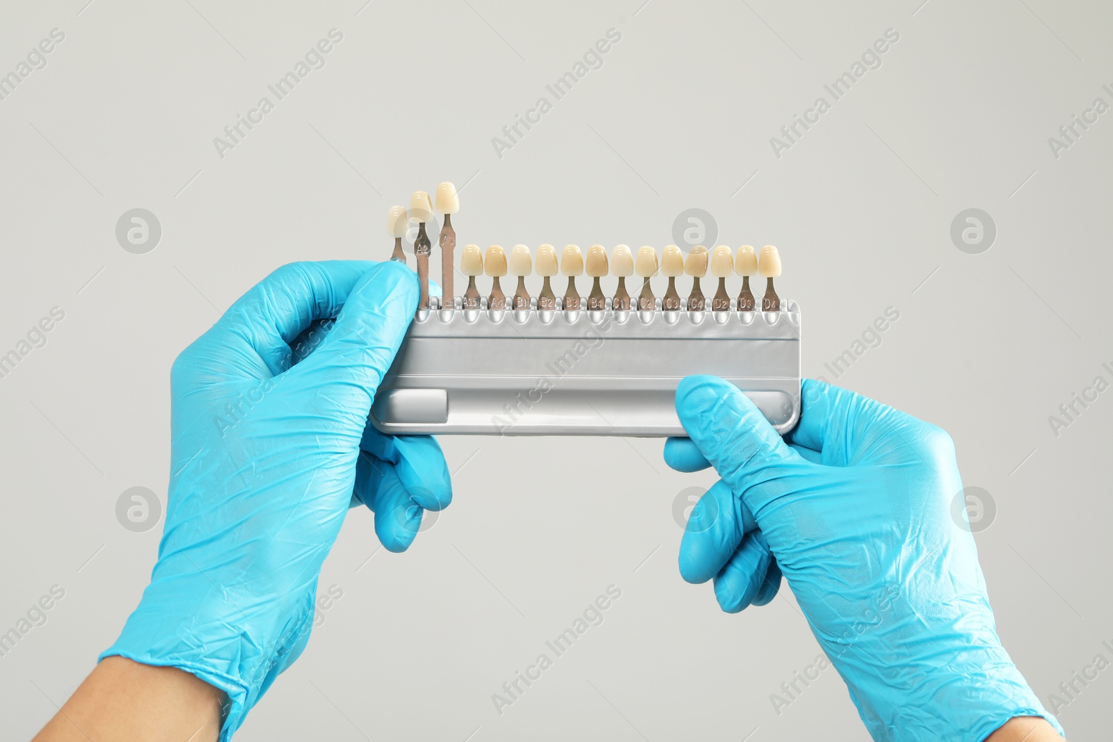 Photo of Doctor with teeth color chart on gray background, closeup. Dental veneers