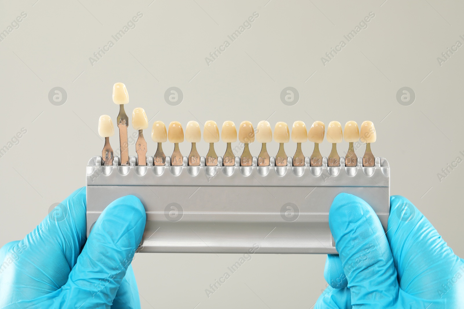 Photo of Doctor with teeth color chart on gray background, closeup. Dental veneers