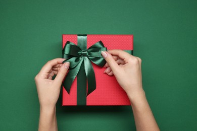 Photo of Woman decorating gift box with bow on green background, top view