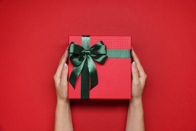 Photo of Woman holding gift box with bow on red background, top view