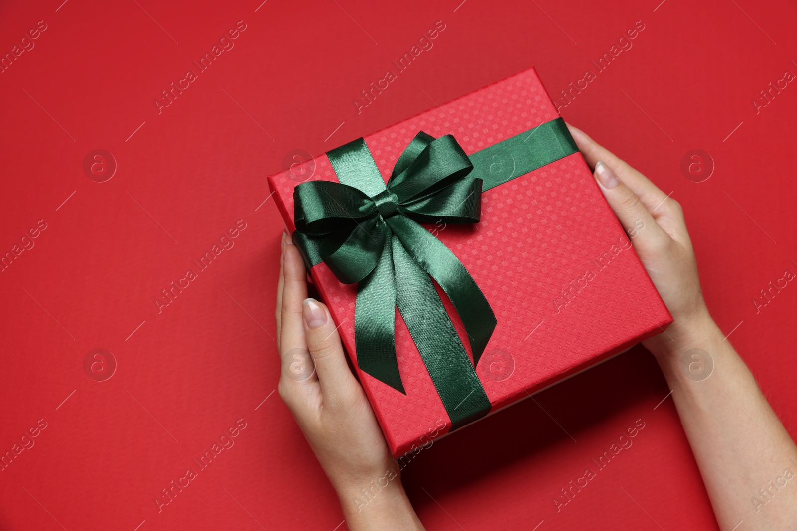 Photo of Woman holding gift box with bow on red background, top view