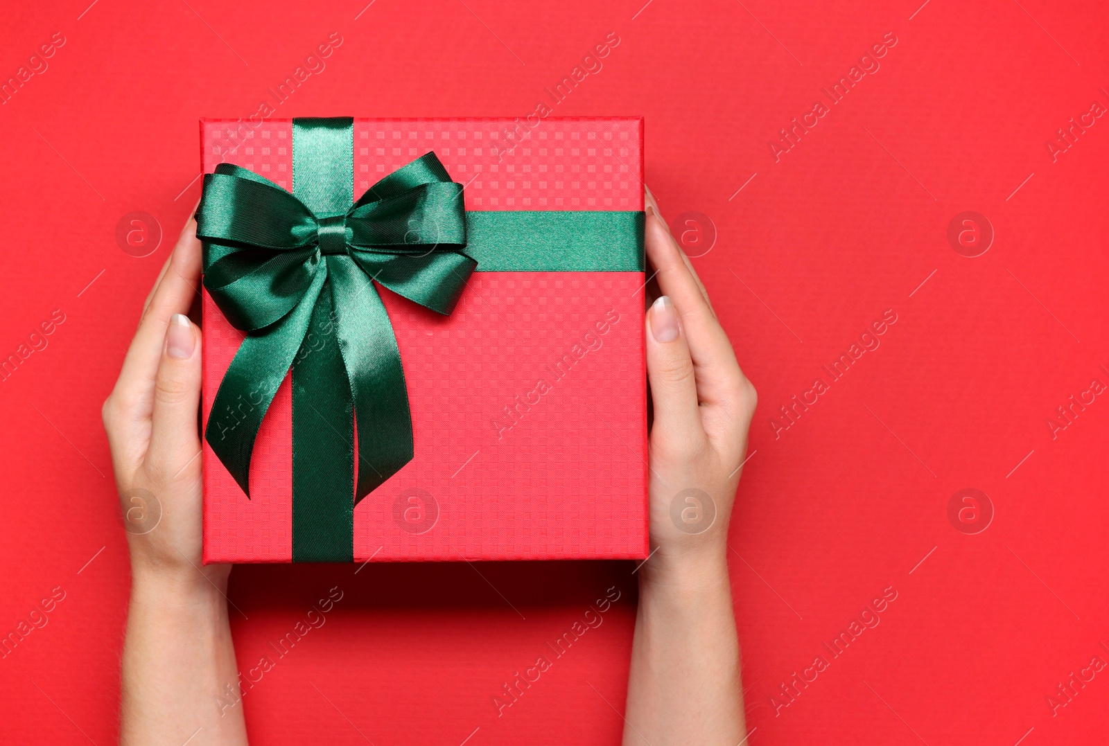 Photo of Woman holding gift box with bow on red background, top view. Space for text